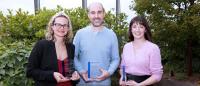 Three award winners standing in front of an outdoor landscape.